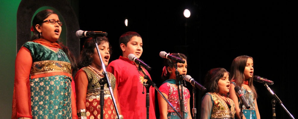 Children singing at microphones in traditional South Asian attire